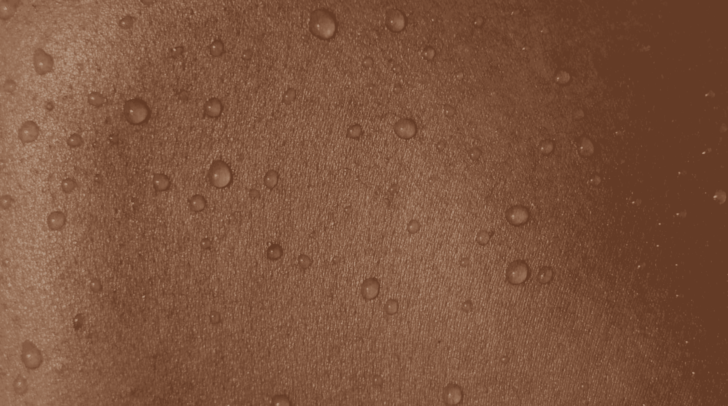 Macro close-up of calm, hydrated skin with fine water droplets in warm terracotta light