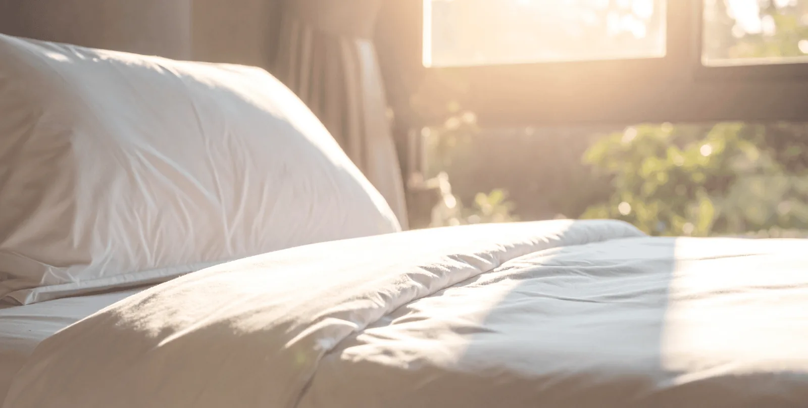 Sunlit bed with soft white linen in a calm morning bedroom